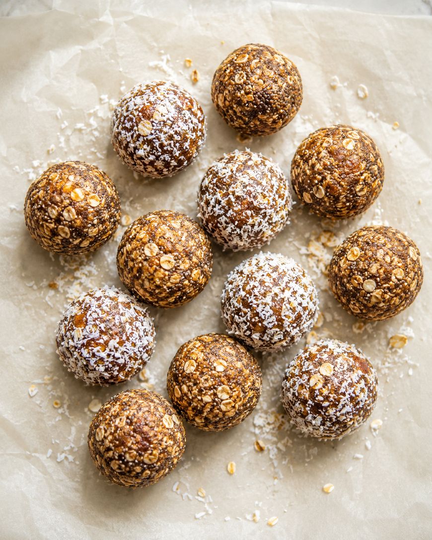 Twelve round energy bites, some coated in shredded coconut, are arranged on parchment paper. The bites have a textured appearance with visible oats.