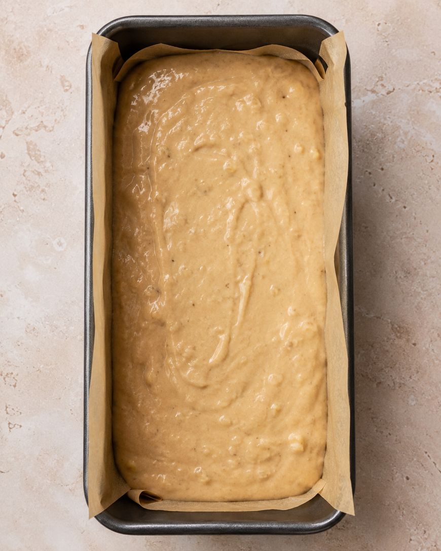 A loaf pan lined with parchment paper is filled with unbaked banana bread batter, ready to go into the oven.